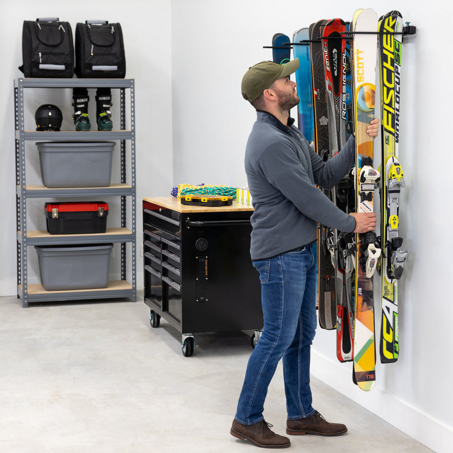Man hanging a pair of skis on a wall ski rack in a garage