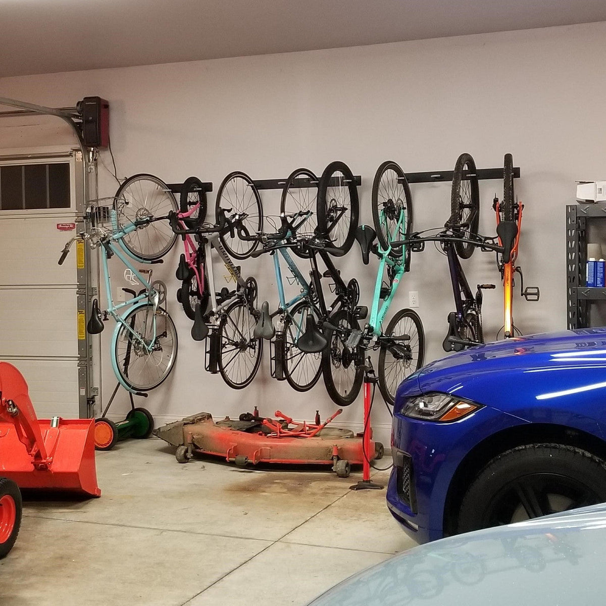Garage wall lined with bikes hanging on wall racks beside a parked car