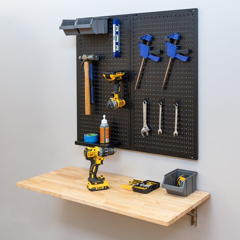 Folding wood workbench below a pegboard holding hand tools and a drill