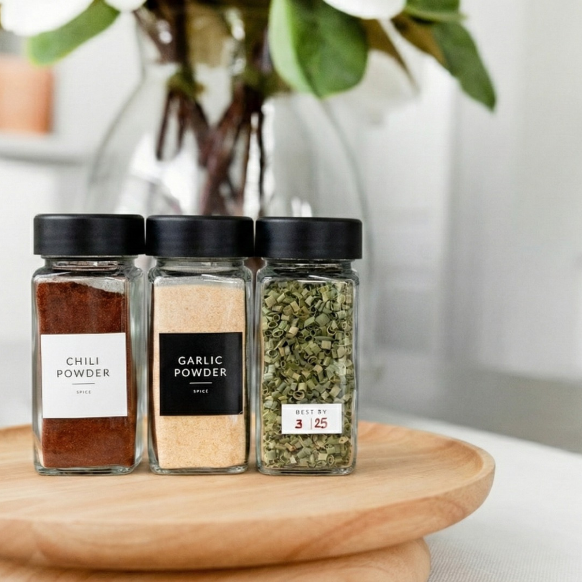 Three labeled square spice jars with black lids on a wooden turntable
