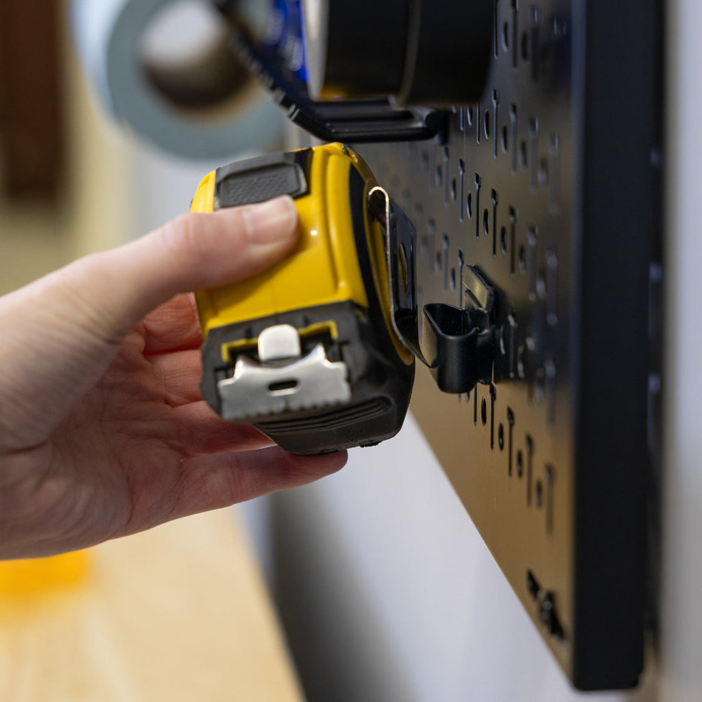 Hand hanging a tape measure on a pegboard hook