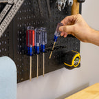Hand placing a screwdriver into a holder on the pegboard