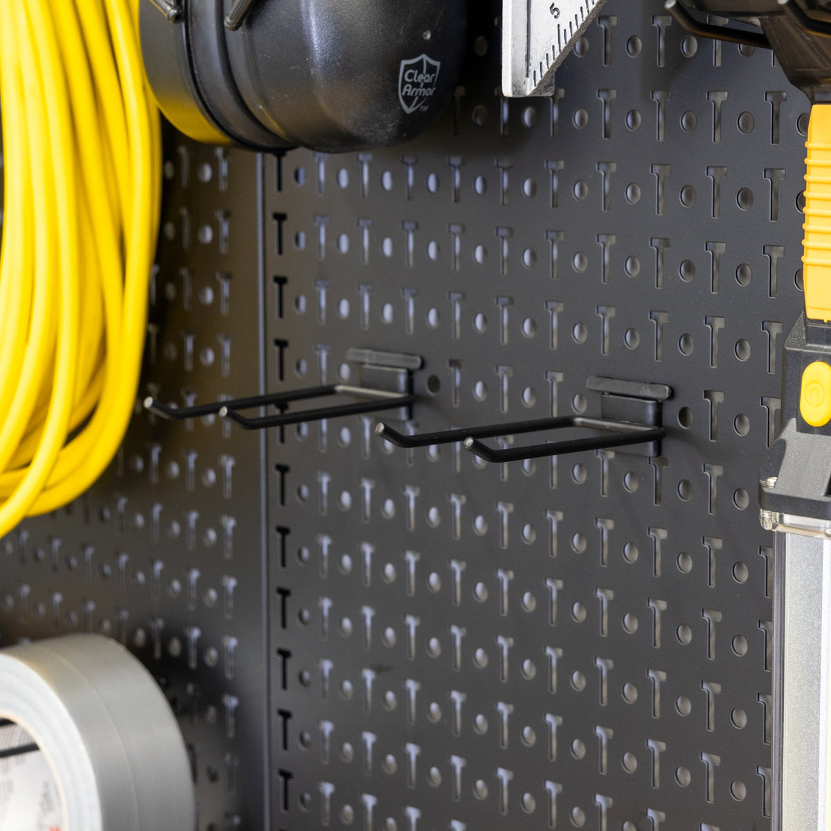 Close-up of pegboard hooks holding an extension cord and tape