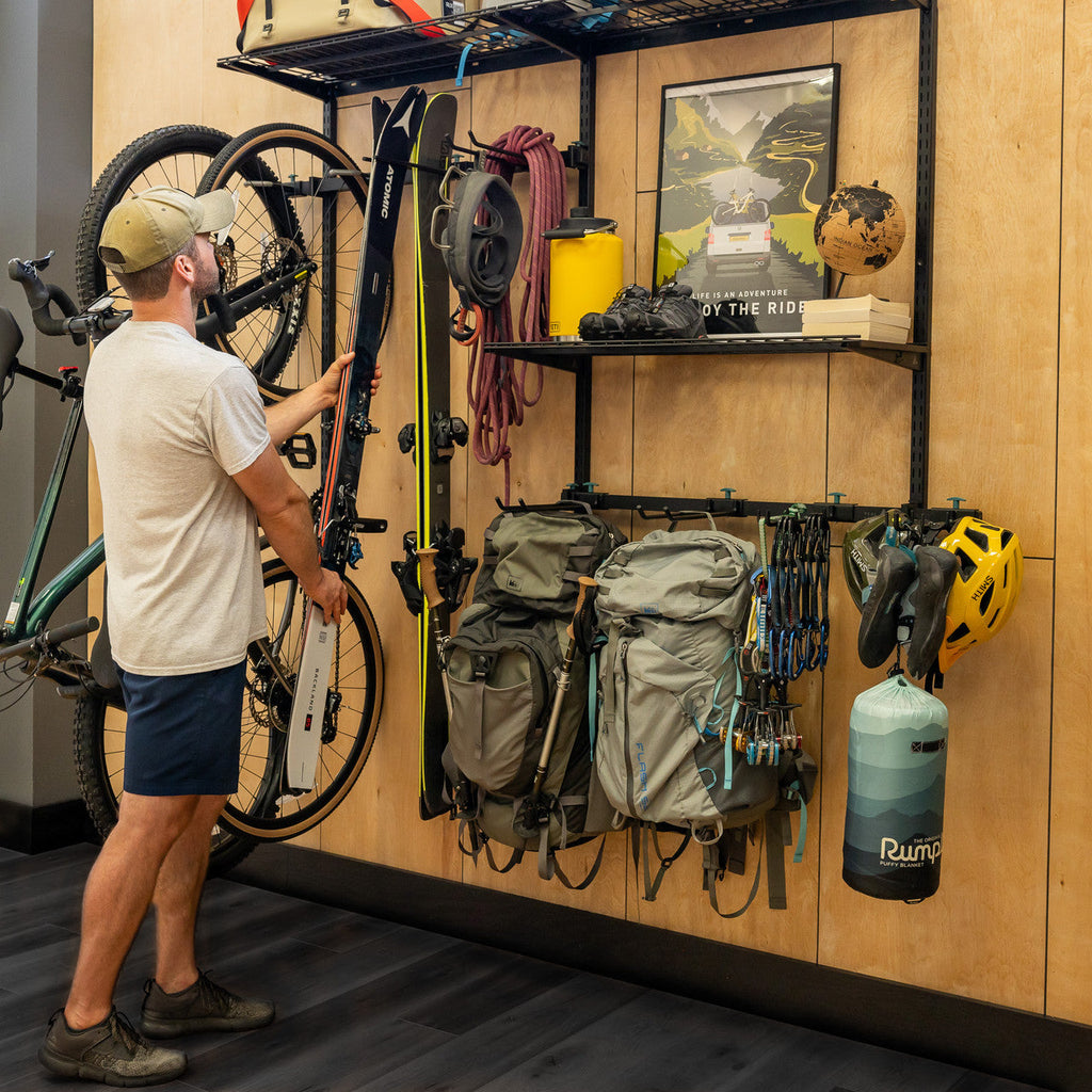 Man hanging a bike on the G-Adventure Pro wall system beside backpacks