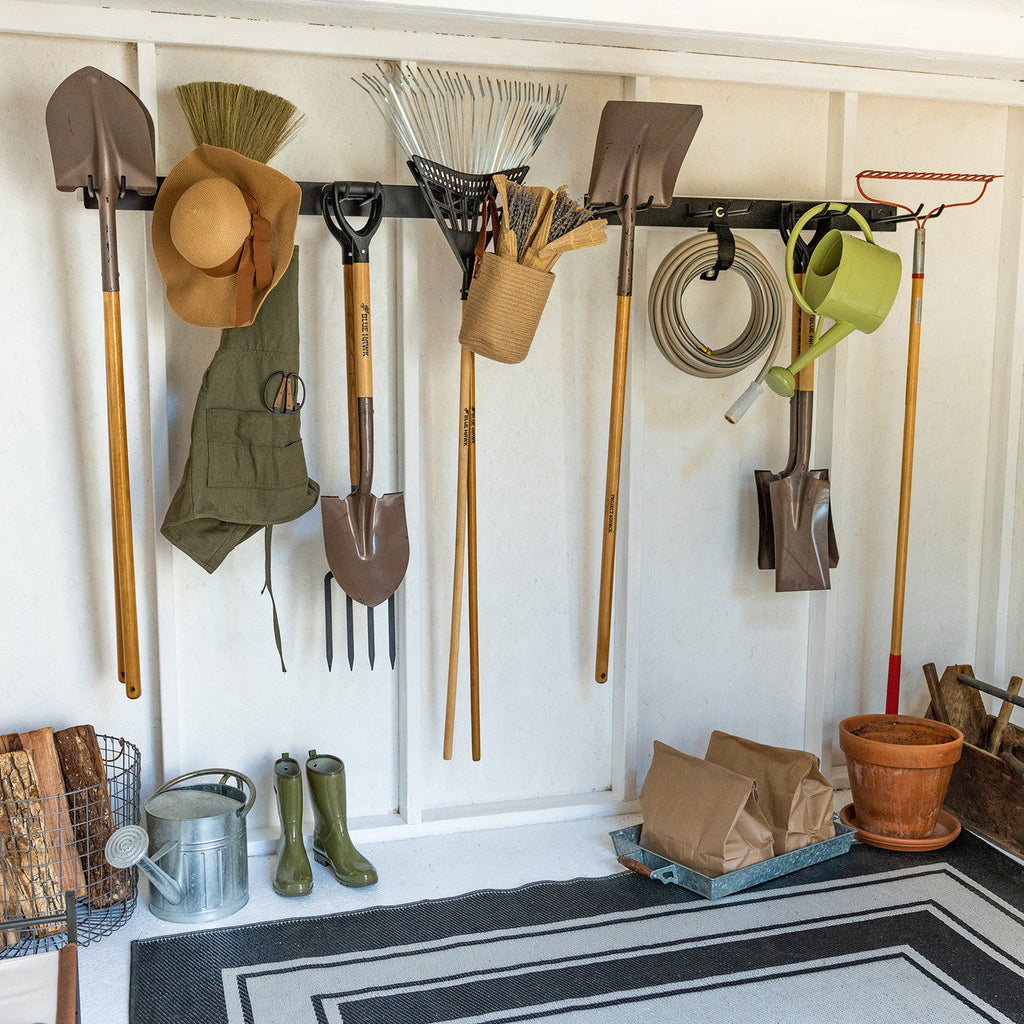 Shed wall with two garden tool organizers holding yard tools above boots and pots