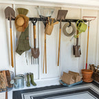 Shed wall with two garden tool organizers holding yard tools above boots and pots