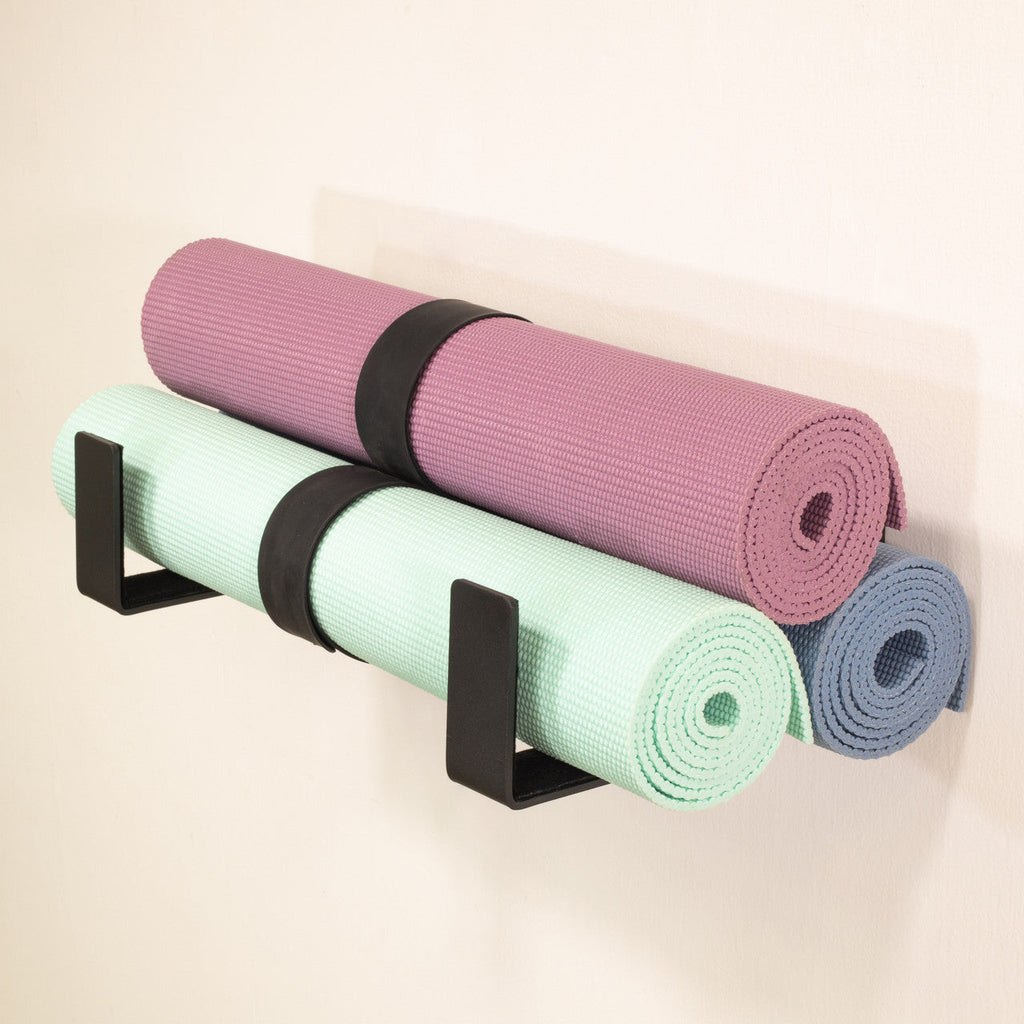 Three yoga mats stored on two minimalist wall hooks