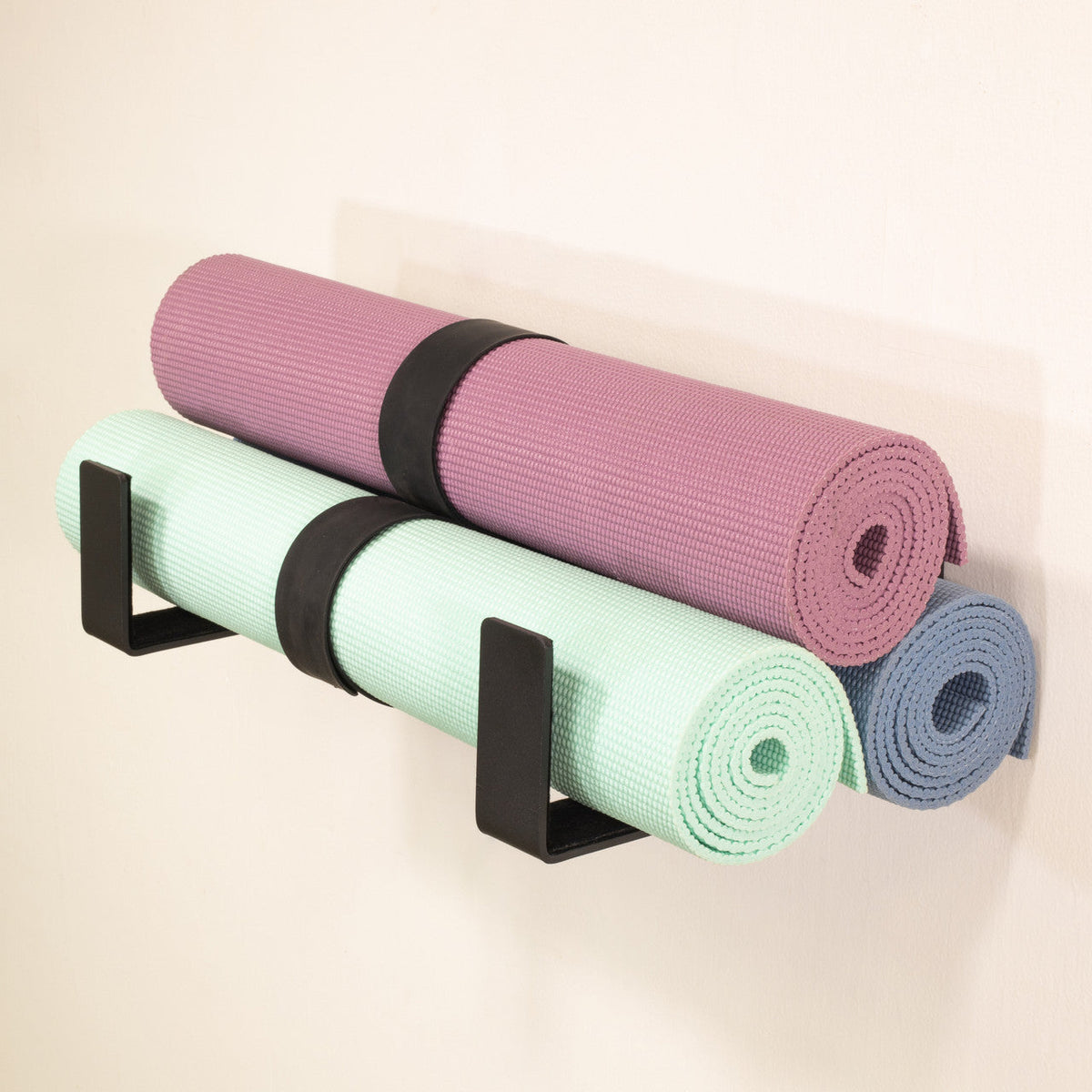 Three yoga mats stored on two minimalist wall hooks