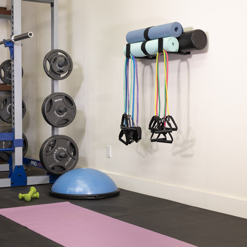 Minimalist wall hooks holding foam rollers and resistance bands in a home gym