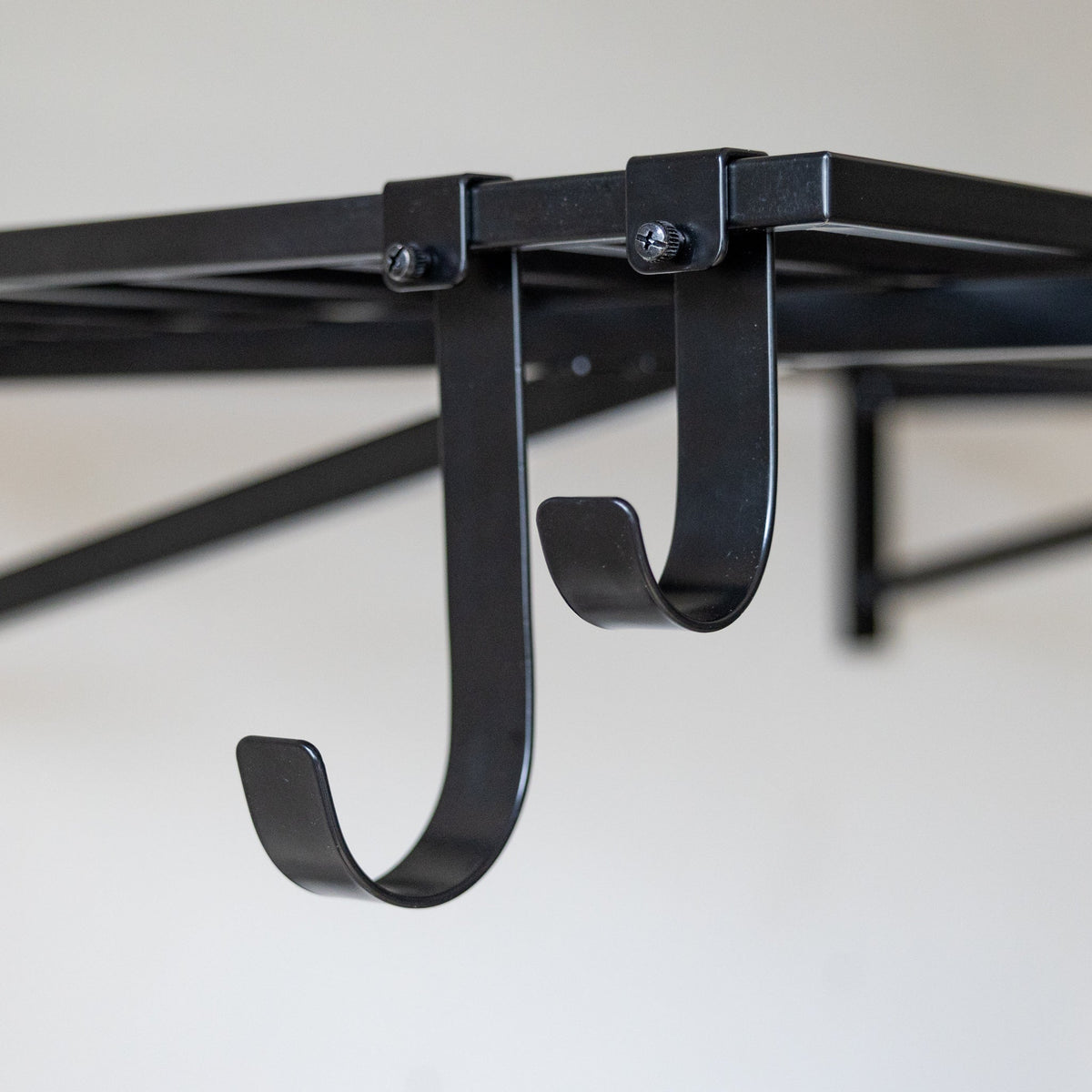 Two black shelf hooks clipped under a wall shelf
