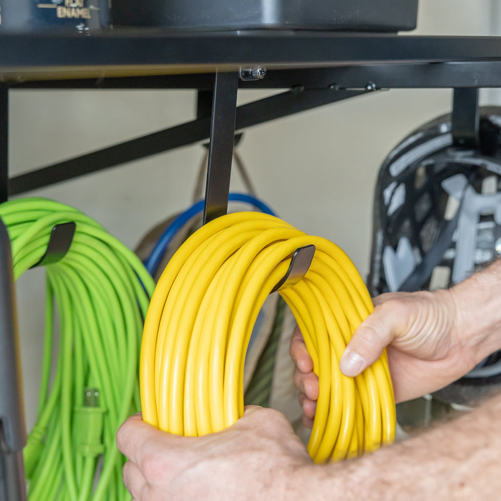 Hand hanging extension cords on shelf hooks under a black shelf