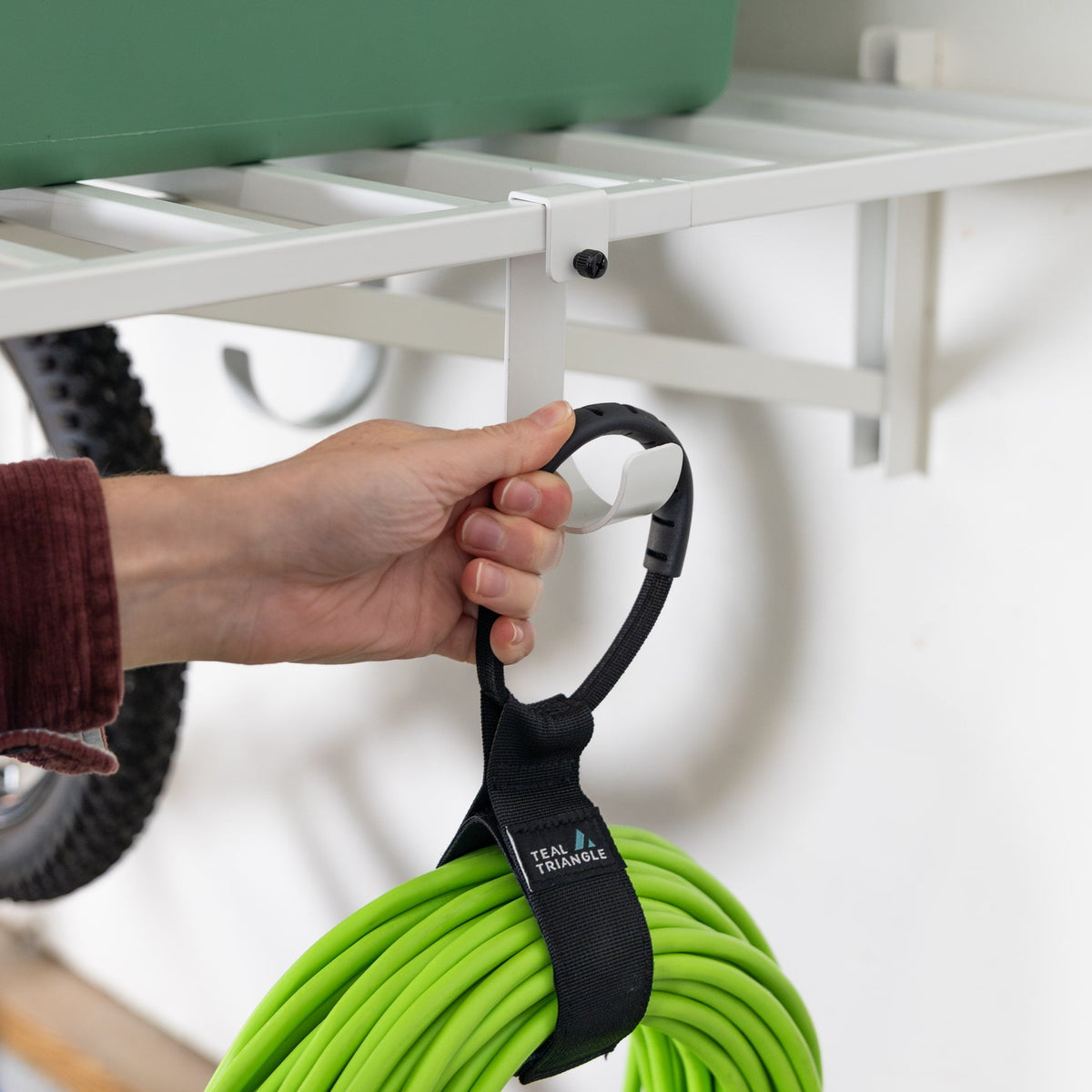 Hand hanging an extension cord with a strap from a hook under a white wall shelf