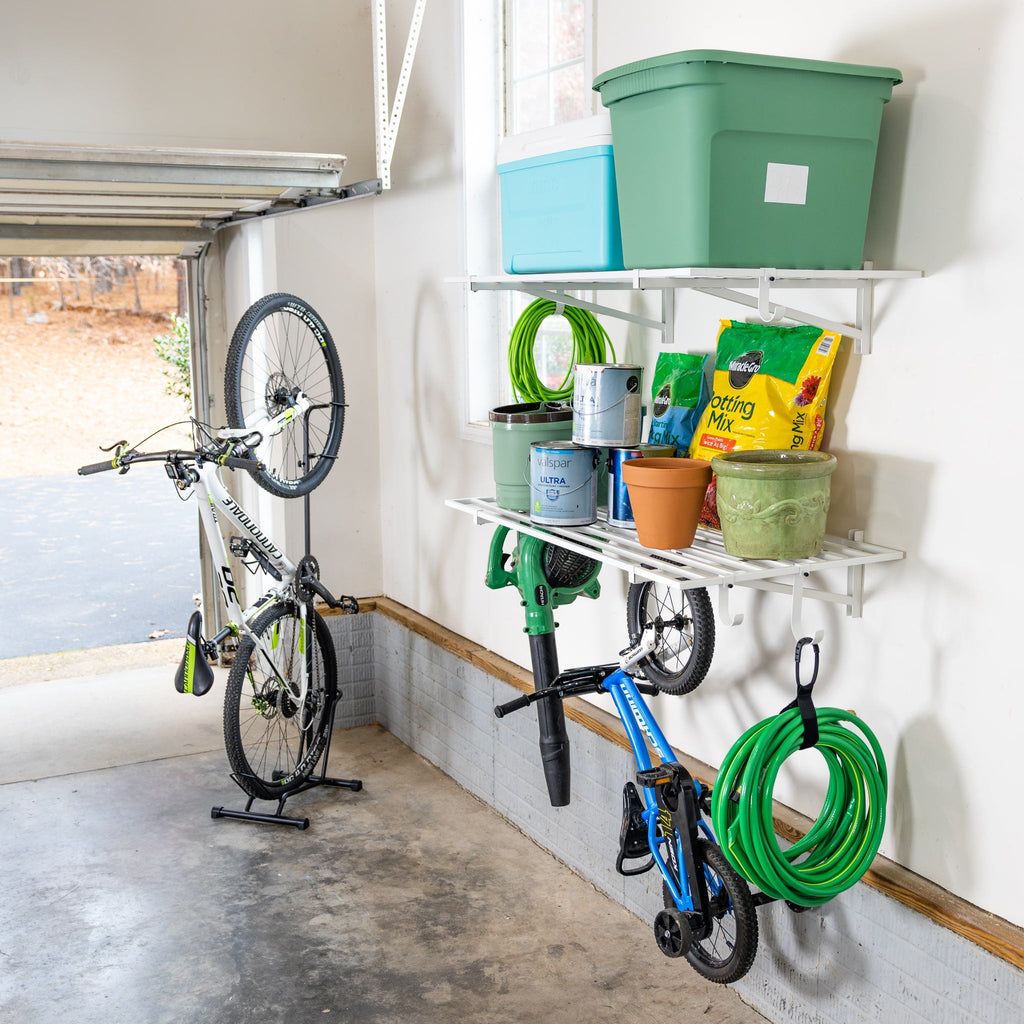 White wall shelves in a garage holding bins and garden supplies, with a bike and hose hung below