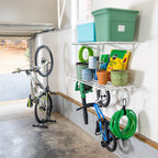 White wall shelves in a garage holding bins and garden supplies, with a bike and hose hung below