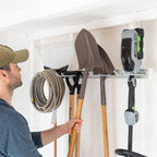 Man hanging a shovel on the gray tool organizer next to a hose and trimmer