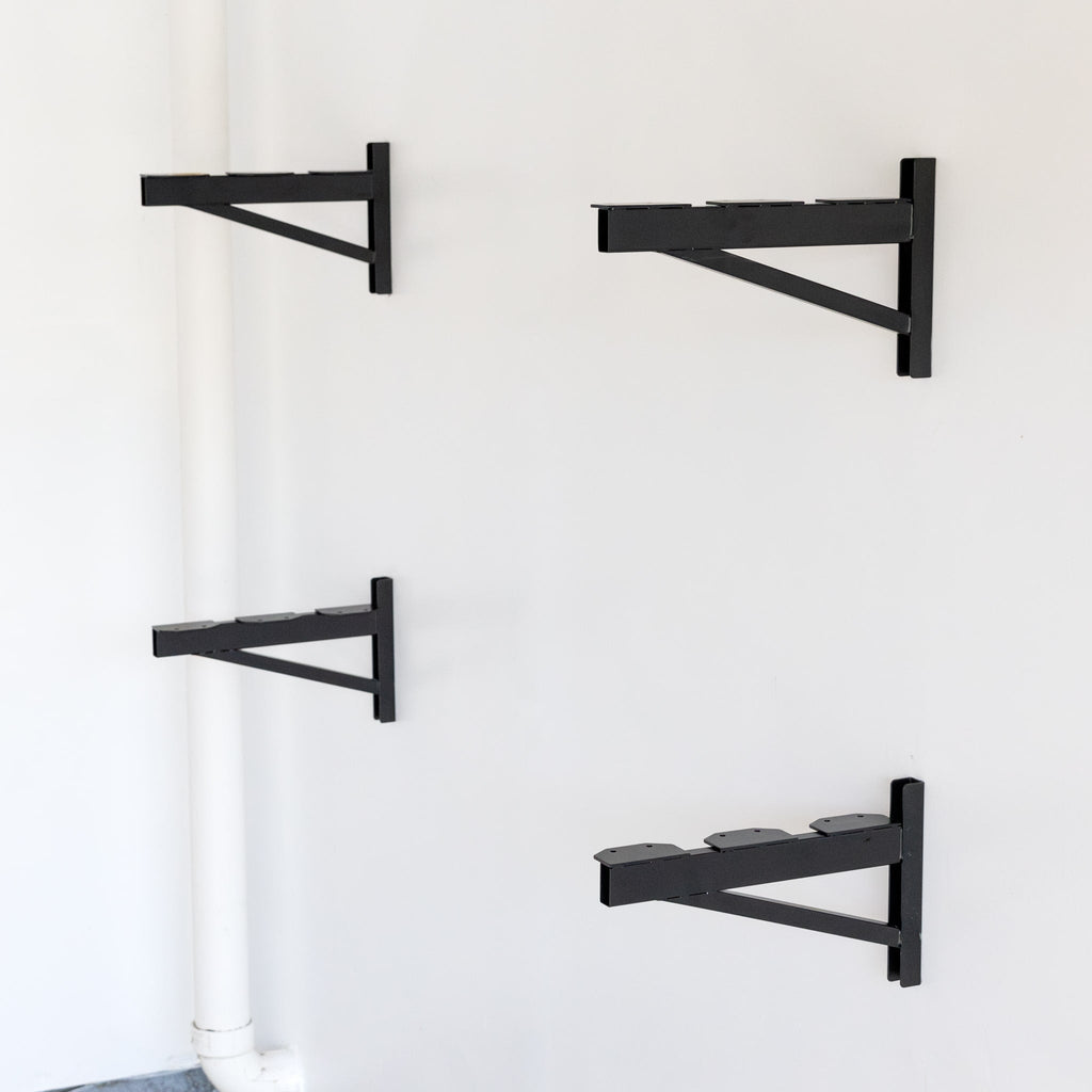 Four black DIY shelf brackets mounted on a wall without shelves