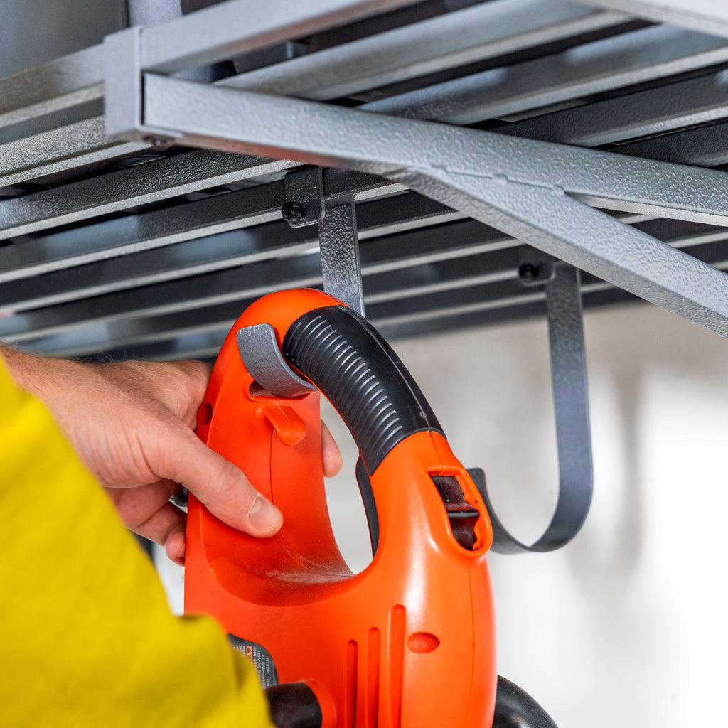 Hand hanging a leaf blower from a hook under a gray wall shelf