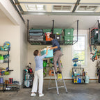 Two people loading bins onto overhead racks from a ladder in a large garage