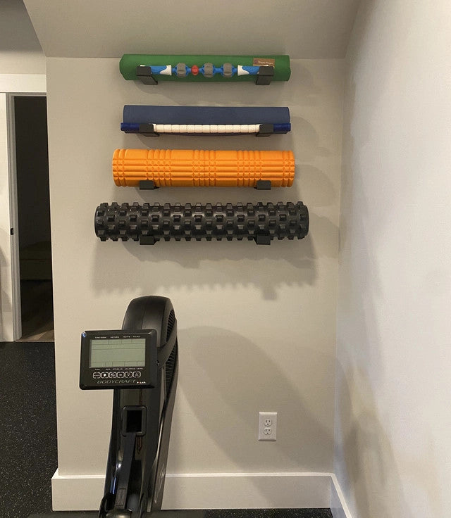 Yoga mats and foam rollers stored on wall hooks above a rowing machine