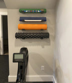Yoga mats and foam rollers stored on wall hooks above a rowing machine