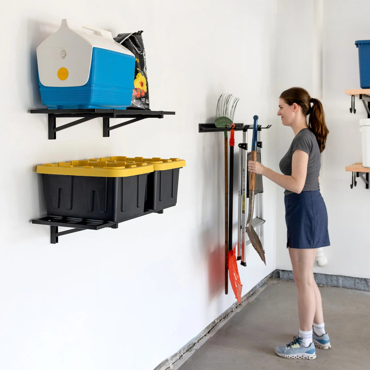 Woman beside two wall shelves holding a cooler and totes in a garage