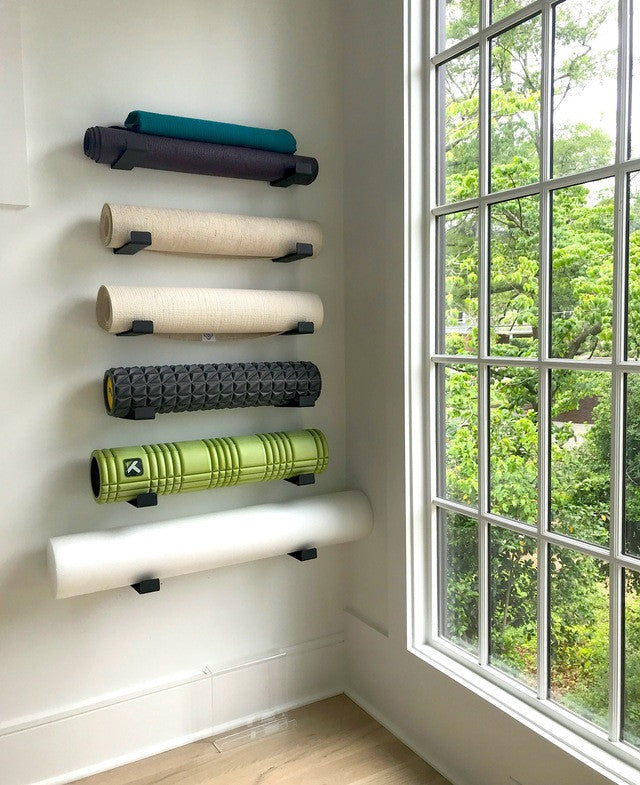 Yoga mats and foam rollers stored on a column of minimalist wall hooks