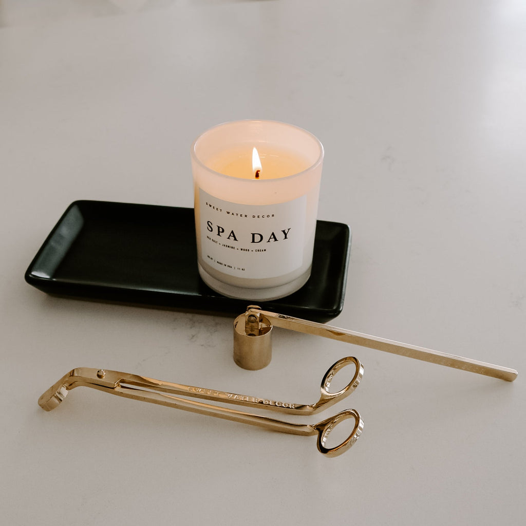 Matte black stoneware tray holding a lit candle beside a gold candle care kit