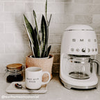 Cream stoneware tray holding a coffee jar and mug beside a coffee maker