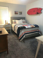 Surfboard displayed on minimalist wall hooks above a bed