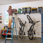 Woman on a ladder placing a bin on a long black wall shelf above hanging bikes