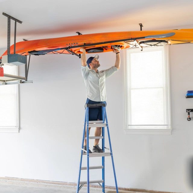 Man on a ladder placing a kayak on the ceiling rack