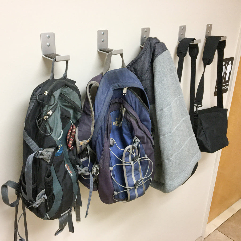 Minimalist wall hooks holding backpacks and bags on a white wall