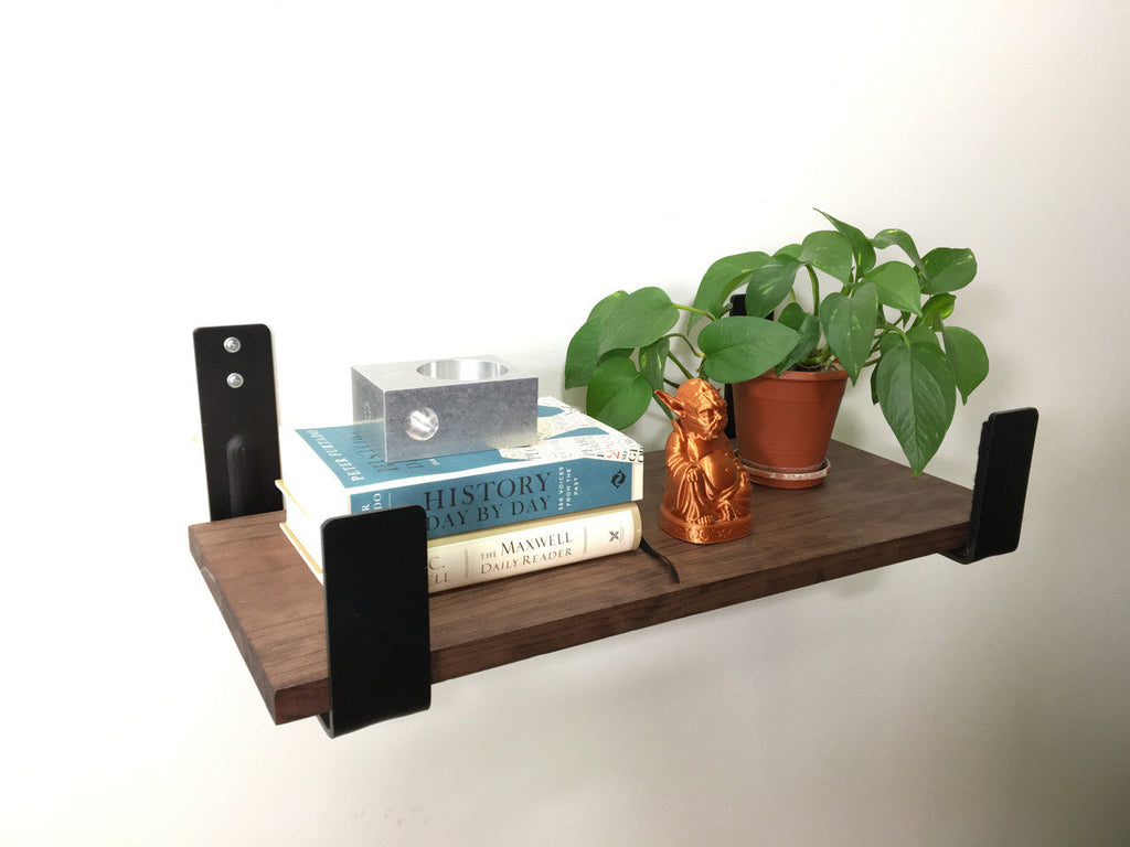 Two minimalist wall hooks holding a wooden shelf with a plant and books