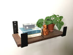 Two minimalist wall hooks holding a wooden shelf with a plant and books