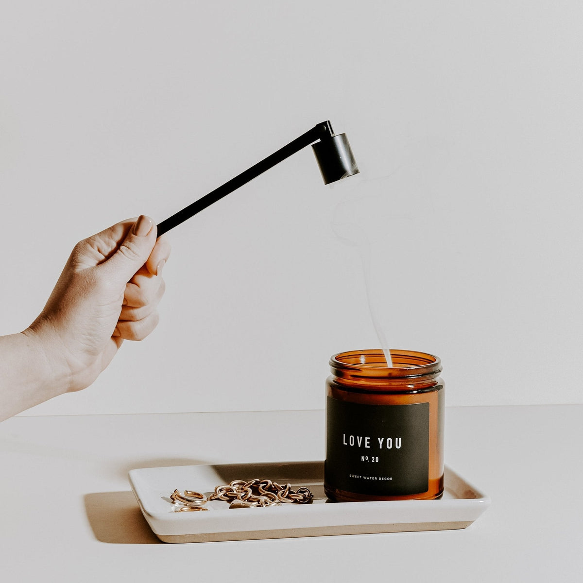 Cream stoneware tray holding an amber jar candle as a hand snuffs it