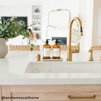 Cream stoneware tray with amber soap dispensers beside a kitchen faucet