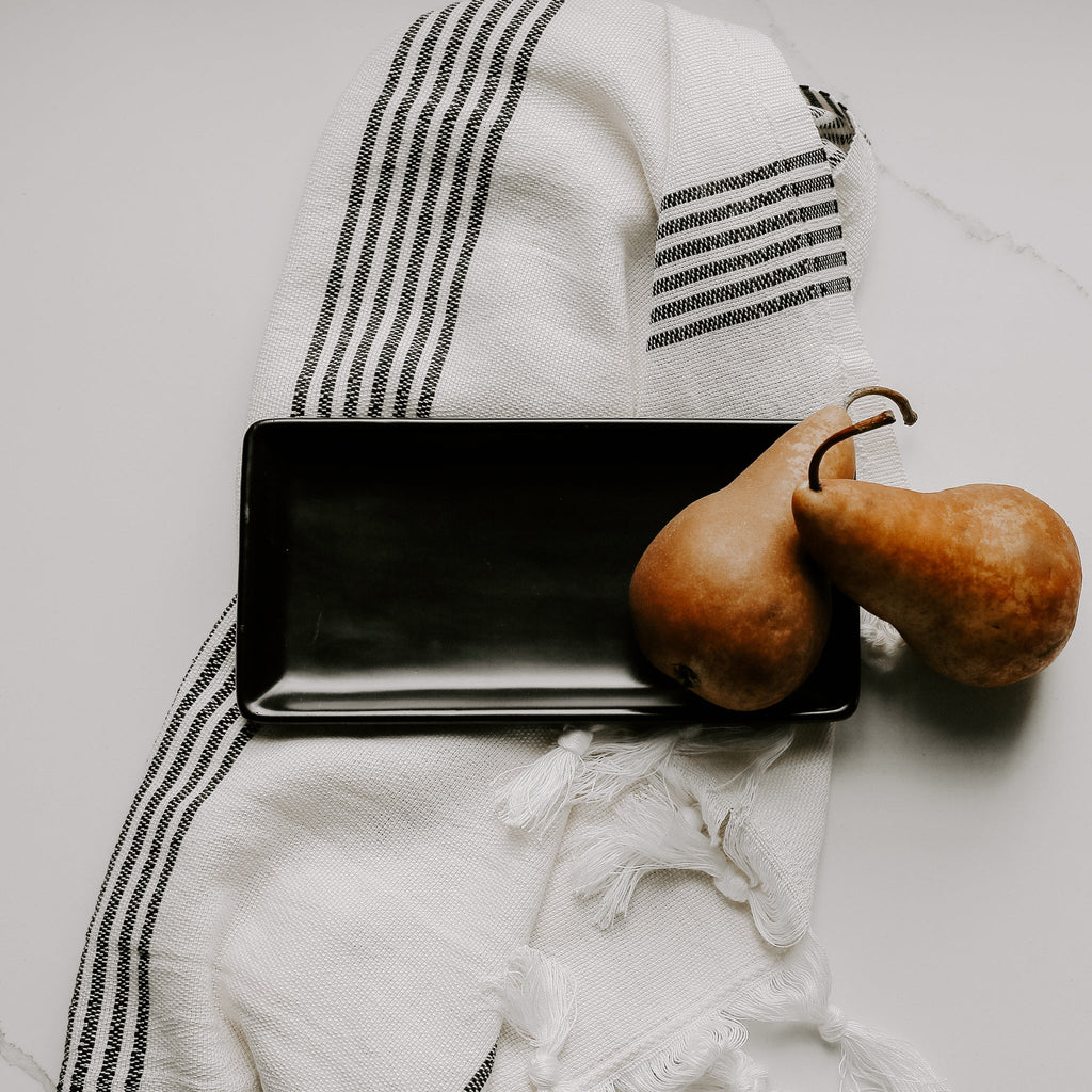 Matte black stoneware tray on a striped towel beside two pears