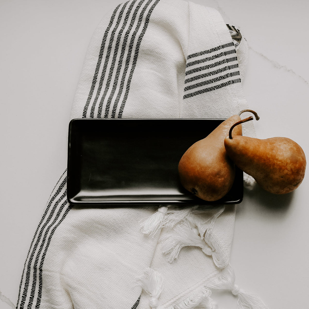 Matte black stoneware tray on a striped towel beside two pears