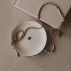 Gold heart jewelry dish holding a gold chain and rings