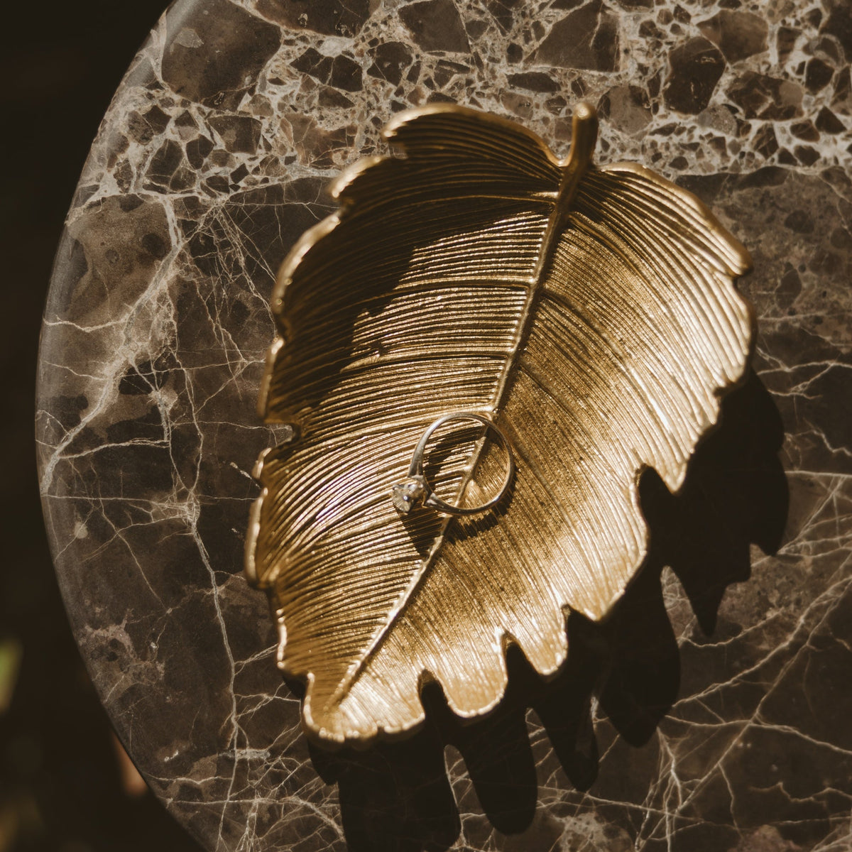 Gold leaf accessory dish holding a ring on a marble surface
