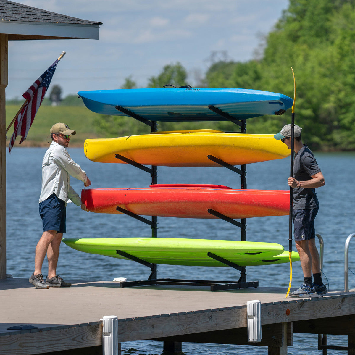 Two men loading four kayaks onto the freestanding rack on a dock