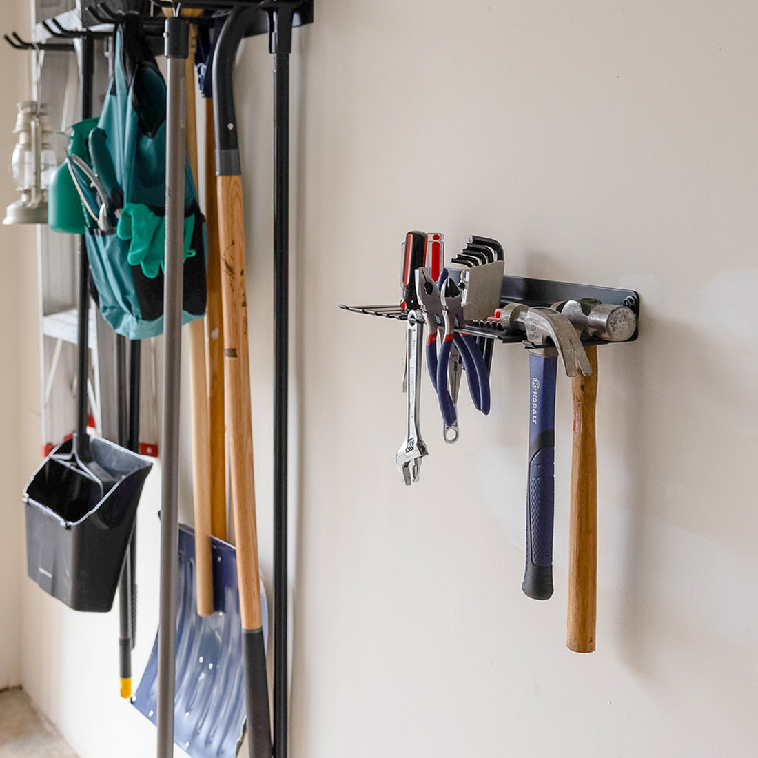 Hand tool organizer on a garage wall holding pliers and a hammer beside hanging yard tools