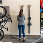 Woman hanging skis on two clear wall racks in a garage