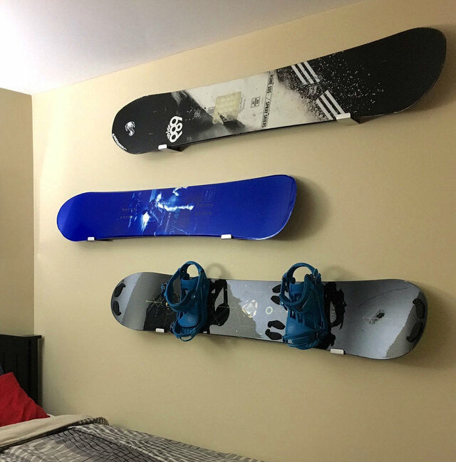Three snowboards displayed on minimalist wall hooks in a bedroom