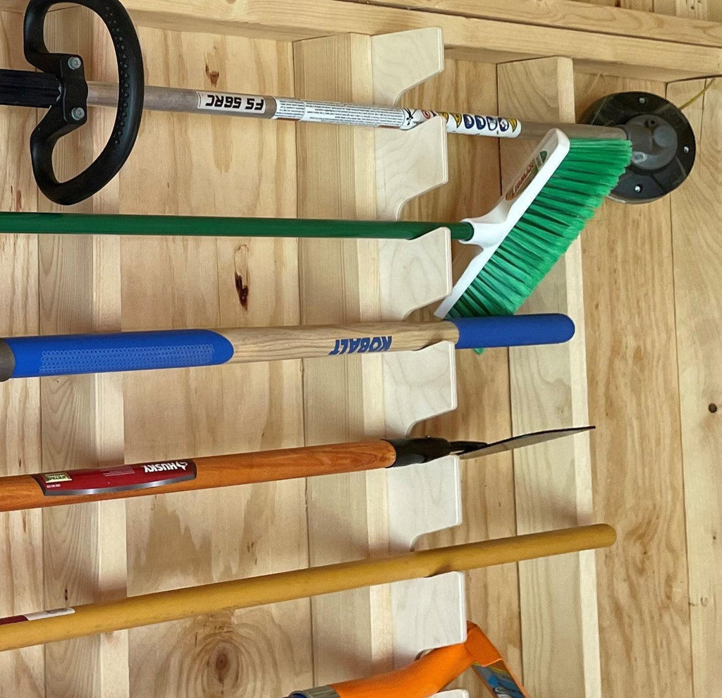 Close-up of a broom and tools resting in the garden tool rack slots