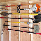 Garden tool rack holding a rake, shovel and trimmer on a shed wall