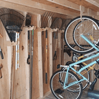 Bikes hanging on wood hooks beside rakes and shovels in a shed