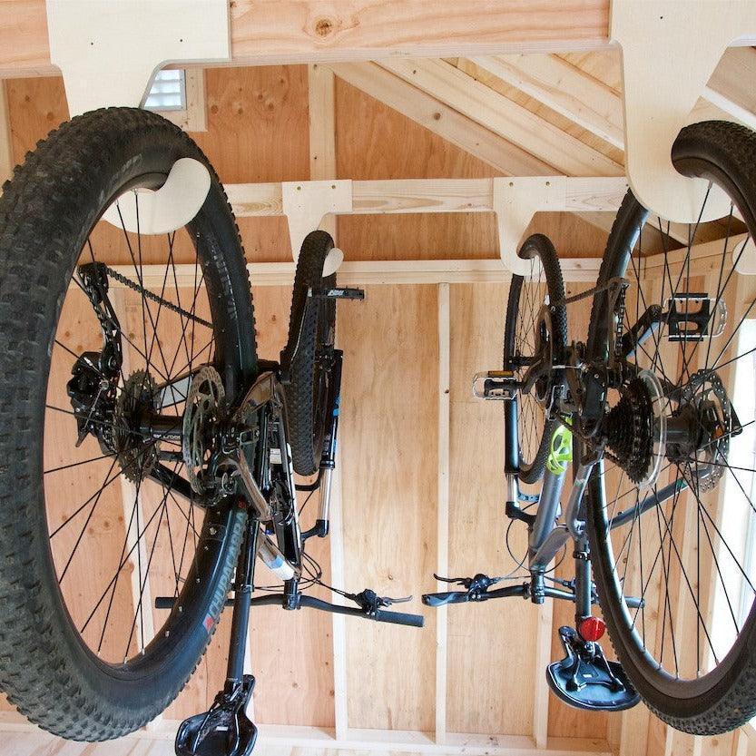 Two bikes hanging by their front wheels on wood bike hooks in a shed