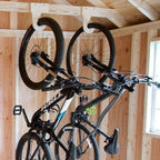 Two bikes hanging on wood bike hooks on a shed wall