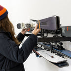 Woman placing a snowboard on the Cascade wall organizer above skis